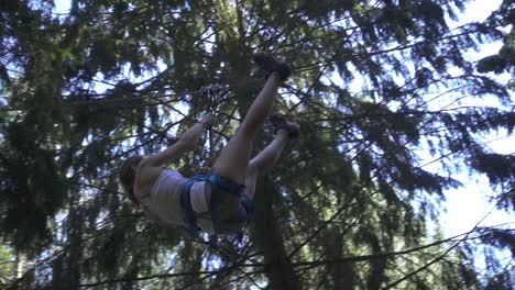 Young-woman-in-safety-equipment-moving-on-rope-with-carbine-in-climbing-park