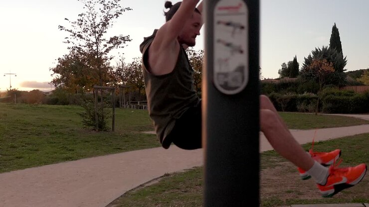 A muscular sportsman is doing muscle ups in a park, with the sunset behind