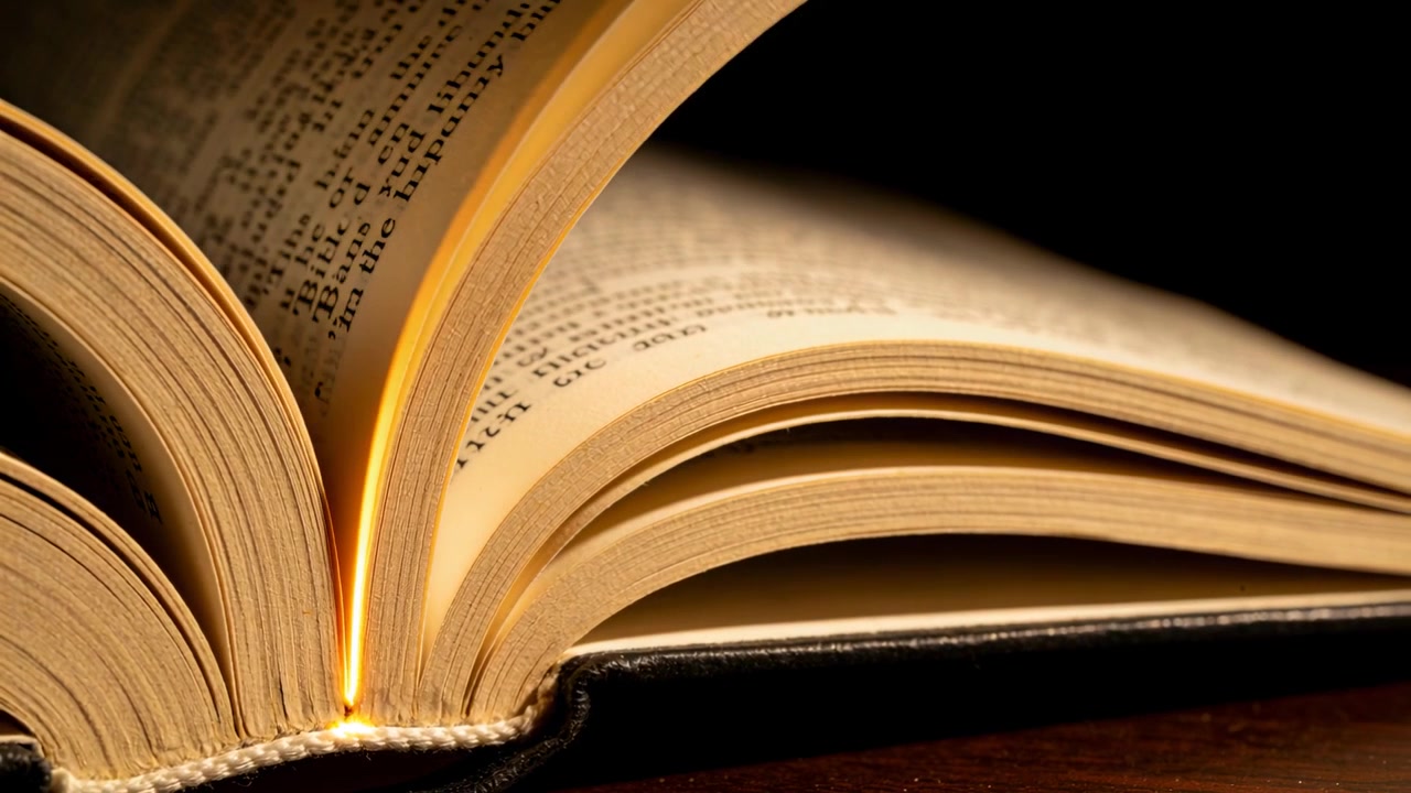 Pagine di un libro con copertina rigida che si sfogliano su un tavolo sotto una lampada con una leggera brezza, rivelando la rilegatura cucita.