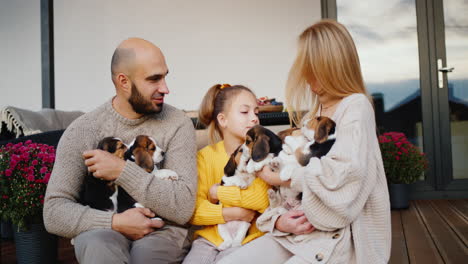 retrato de una familia feliz con el telón de fondo de su casa. mamá, papá e hija - sosteniendo varios cachorros de beagle en sus manos