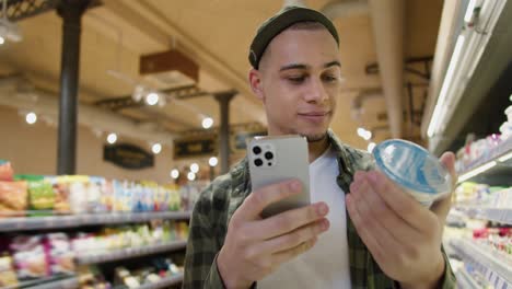 Young-man-shopping-in-supermarket,-reading-product-information-comparing-in-internet