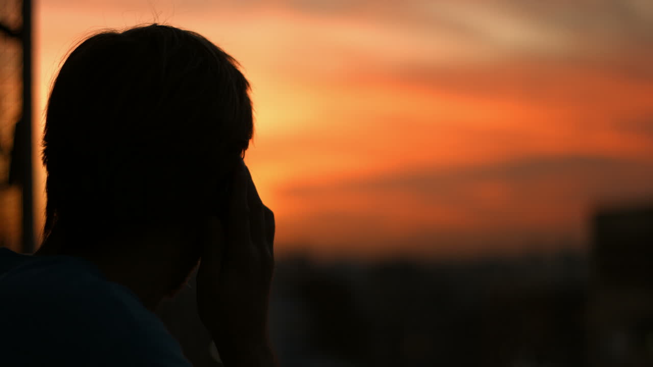 Silhueta de uma Pessoa Falando ao Telefone Contra um Céu Vibrante de Pôr do Sol