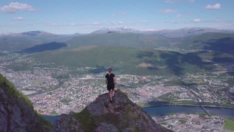 Woman-walking-at-the-top-of-a-mountain-with-mountainous-city-background-panoramic-horizon-aerial-stunning-drone-shot