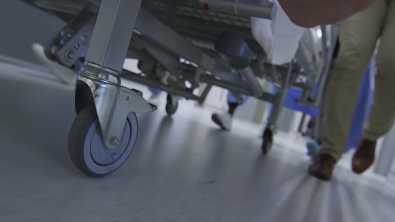 Piedi di medici che camminano lungo un corridoio trasportando un paziente su un letto a rotelle.