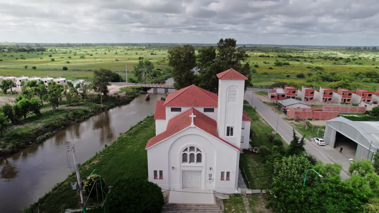 Drone moving backwards over the residential area and church in Punta Lara, with the surrounding natural landscape and canal visible.