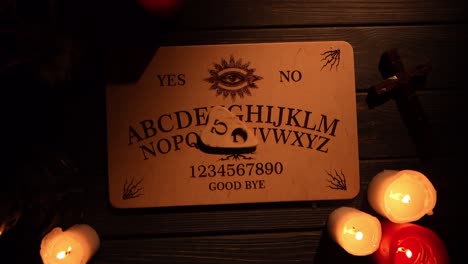 close up video of a wooden ouija board on a table surrounded by candles and a cross in a muffed - close up video of a wooden ouija board on a table. wax candles and a cross around. the planchette is slowly moving across the board, spelling out words and numbers. creative mystical content