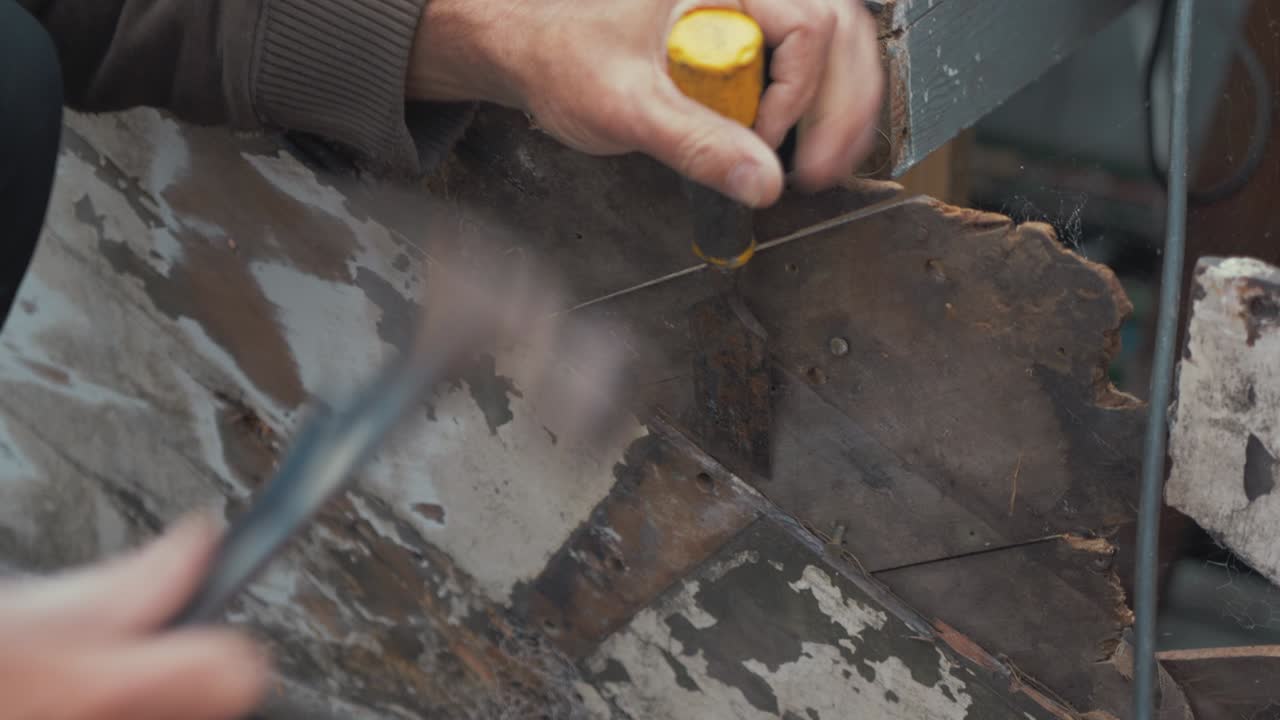 Carpenter using chisel to prise diagonal mahogany planking apart