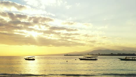 Beautiful-heaven-with-glowing-sunlight-through-hanging-clouds-over-calm-sea-surface-with-anchored-boats-on-bay-of-tropical-island-in-Bali