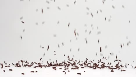 Brown-chocolate-sprinkles-ice-cream-topping-falling-in-slow-motion-and-bouncing-before-settling-into-pile-on-white-backdrop