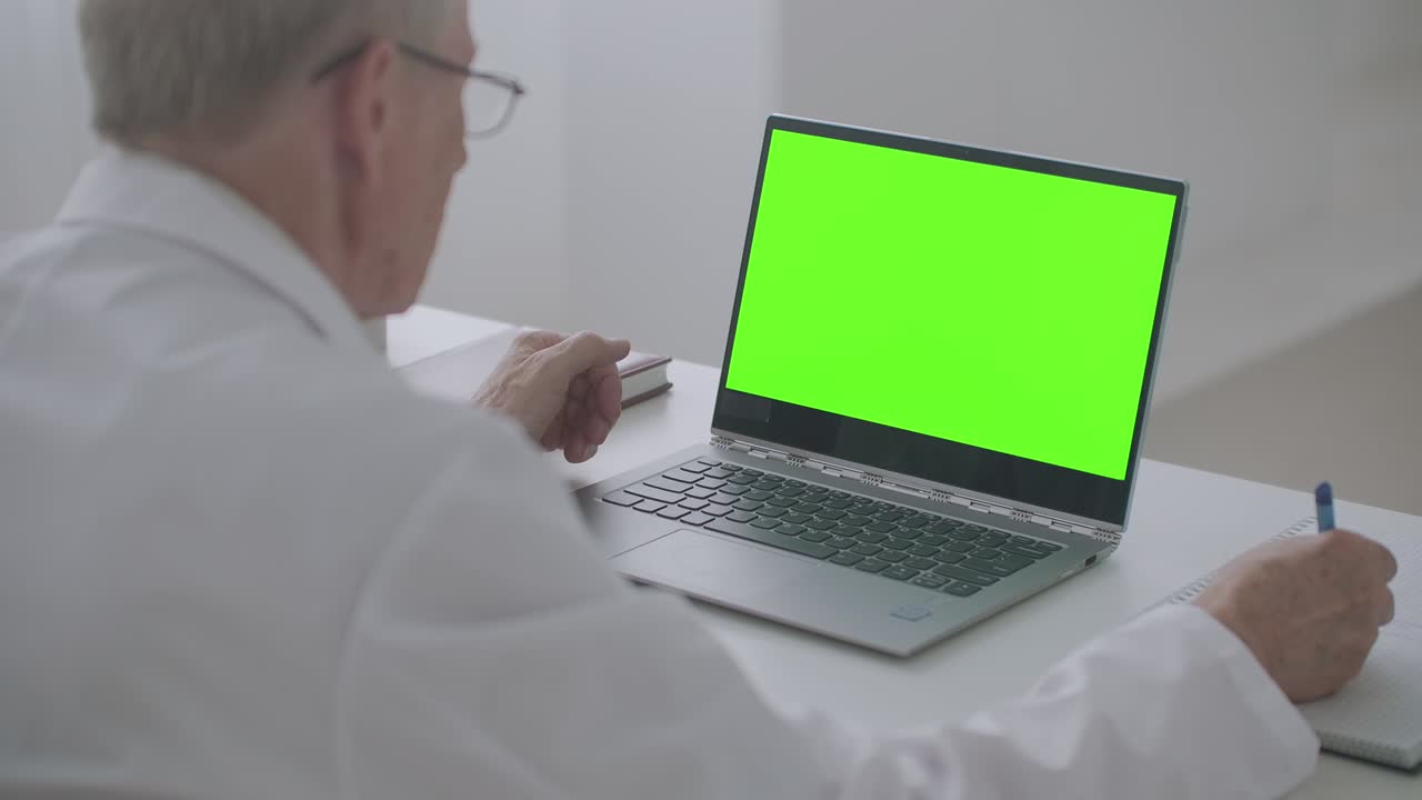 portátil con pantalla verde en la mesa del médico de trabajo, el hombre está mirando la pantalla y escribiendo notas, concepto de aprendizaje electrónico