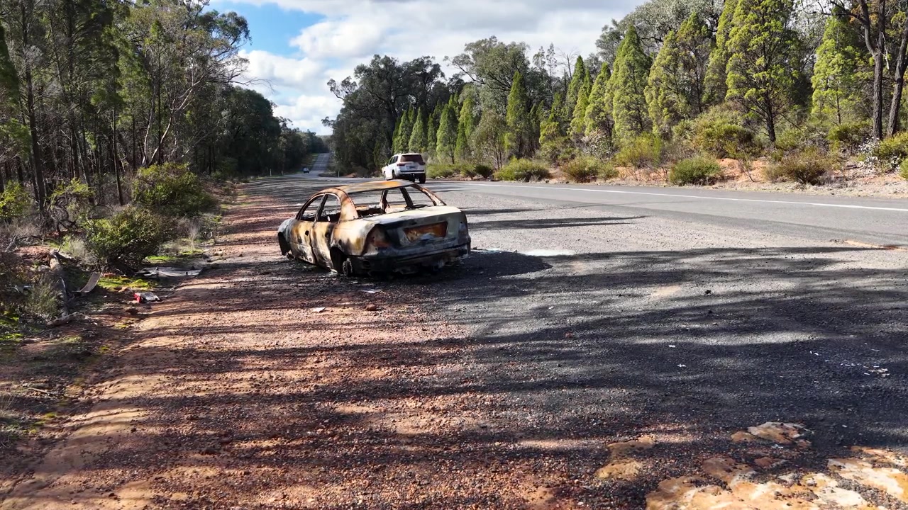 Vidvinkelbillede af et udbrændt sedanvrag ved siden af en motorvej i Goonoo Forest, Australien.