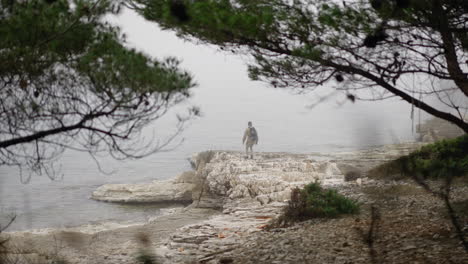 Young-man-jumping-to-the-edge-of-rocky-beach-and-looking-into-distance