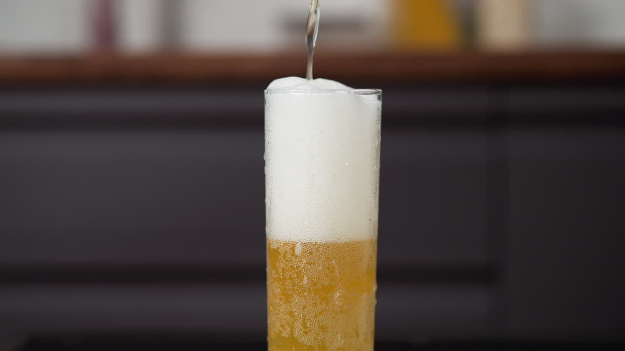 Frothy golden beer pouring into a tall glass with rising bubbles and foam head