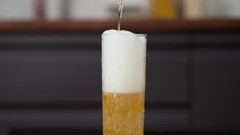 frothy golden beer pouring into a tall glass with rising bubbles and foam head