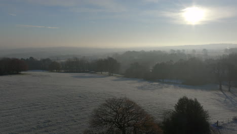 Rising-Establishing-Aerial-Drone-Shot-Over-Fields-and-Trees-in-Winter-on-Frosty-Misty-Morning-in-UK