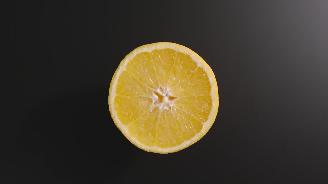 Metà di un'arancia ruota su una superficie nera. Vista dall'alto. Stop motion