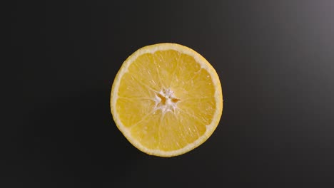 la mitad de una naranja gira sobre una superficie negra. vista superior. detener el movimiento
