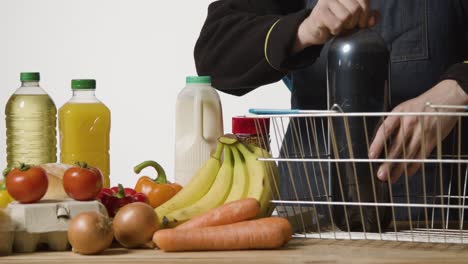 studio shot of shop worker at checkout putting basic food items into supermarket wire shopping basket