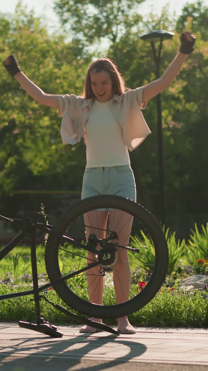 una joven dama saltando y bailando alegremente junto a su bicicleta al revés, expresando felicidad y emoción en un entorno al aire libre iluminado por el sol, con la vegetación borrosa creando un telón de fondo vibrante