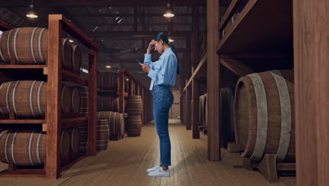 full body side view of an asian female professional worker standing with her phone in cellar of winery, she is nodding her shead with dissapionted