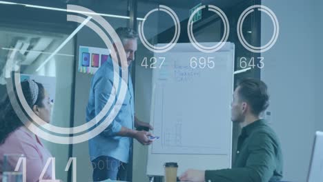 Animation-of-loading-circles,-numbers-over-diverse-manager-explaining-strategy-on-board-to-coworkers