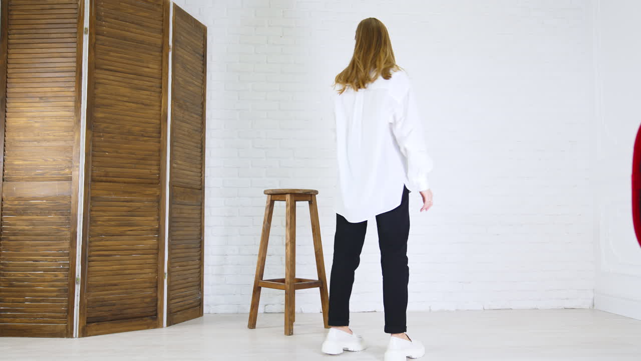 Blonde young woman demonstrates white shoes. Lady in white shirt and black pants walks back and forth showing footwear.