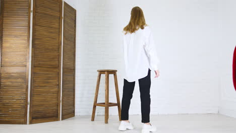 blonde young woman demonstrates white shoes. lady in white shirt and black pants walks back and forth showing footwear.