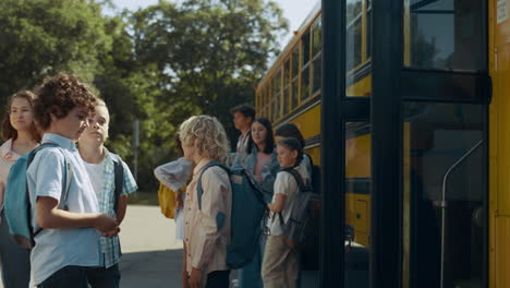 diverse students standing together at schoolbus. boys talking near open door.