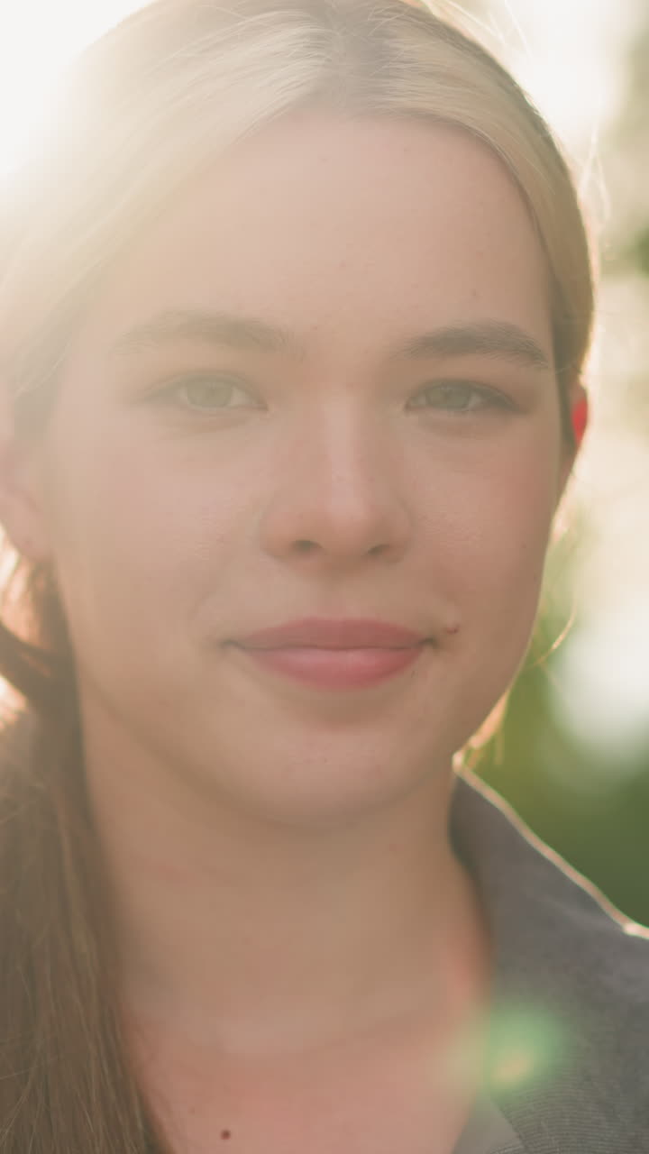 primer plano de una mujer mirando directamente a la cámara con una suave sonrisa, su rostro suavemente iluminado por la cálida luz natural del sol desde atrás, la vegetación borrosa en el fondo