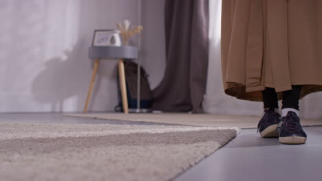 close up of muslim woman at home taking off shoes and laying down prayer mat on floor