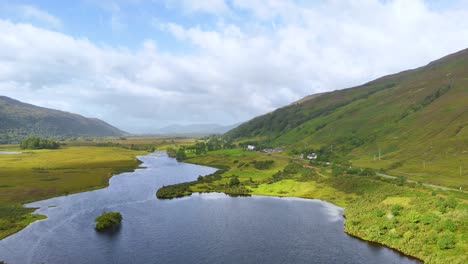 aerial camera smoothly glides above a winding river, grassy fields, and green hills under partly cloudy daylight in the scottish highlands