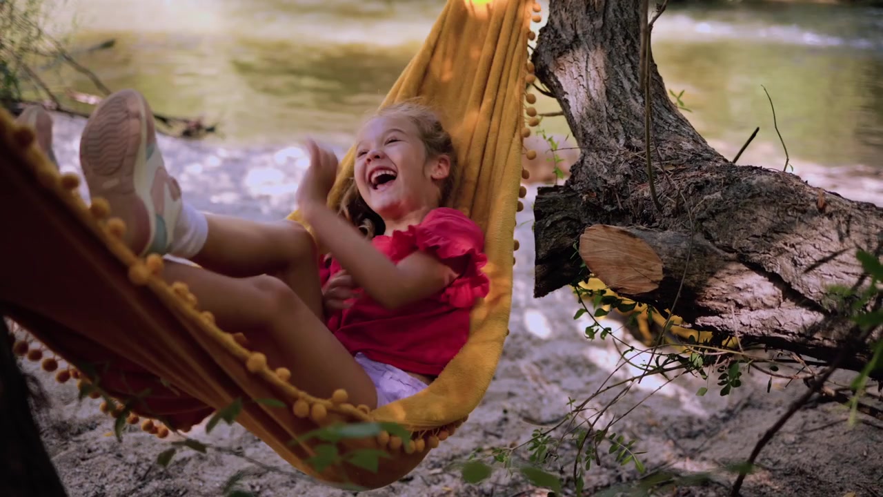 Bambina felice che ride su un'amaca in riva al fiume.