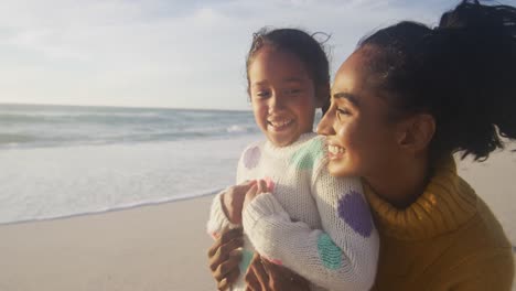 portrait of happy hispanic mother and daughter embracing on beach at sunset