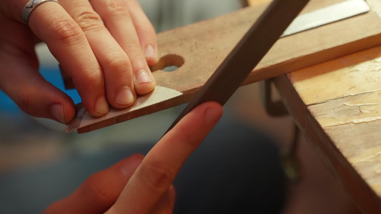 A person diligently shapes a piece of wood using hand tools, focusing on precision and detail in a workshop filled with tools and materials.