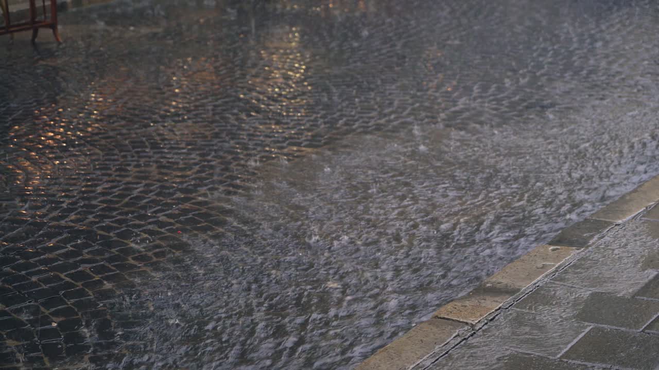 rain drops are turning into a stream of water which flowing on the pavement. It's raining in the city