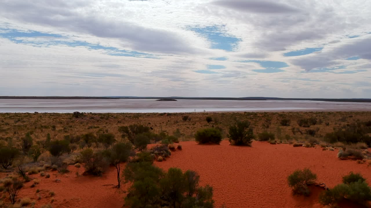 drone volando sobre una pista de arena roja que conduce al lago salado interior
