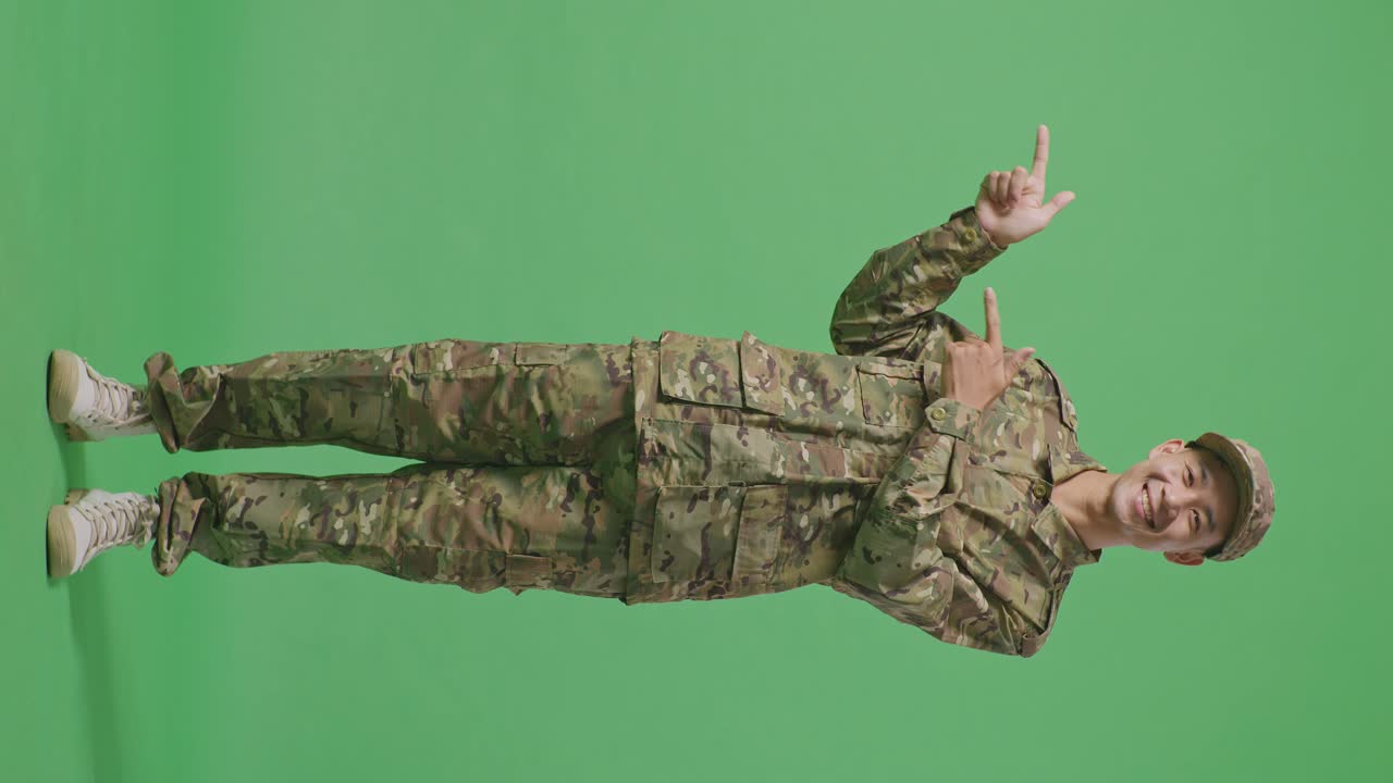 Full Body Of Asian Man Soldier Smiling And Pointing To Side While Standing In The Green Screen Background Studio
