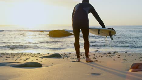 side view of mid-adult caucasian male surfer placing surfboard on sand at the beach 4k