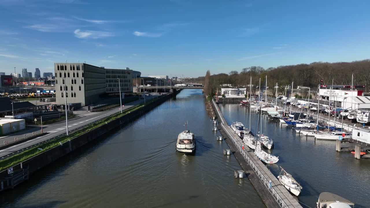 Zoom in aerial view of a boat sailing through marina canal in Brussels, Belgium, surrounded by docked yachts and buildings