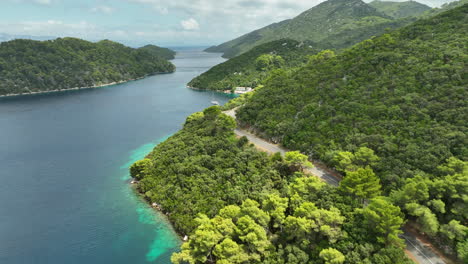 Drone-dolley-shot-over-the-hilly-landscape-of-Mljet-island-where-a-car-drives-along-the-coastal-road