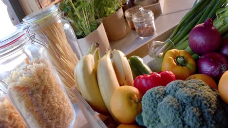 crate of organic vegetables and storage jars of food on countertop in sunny kitchen, slow motion