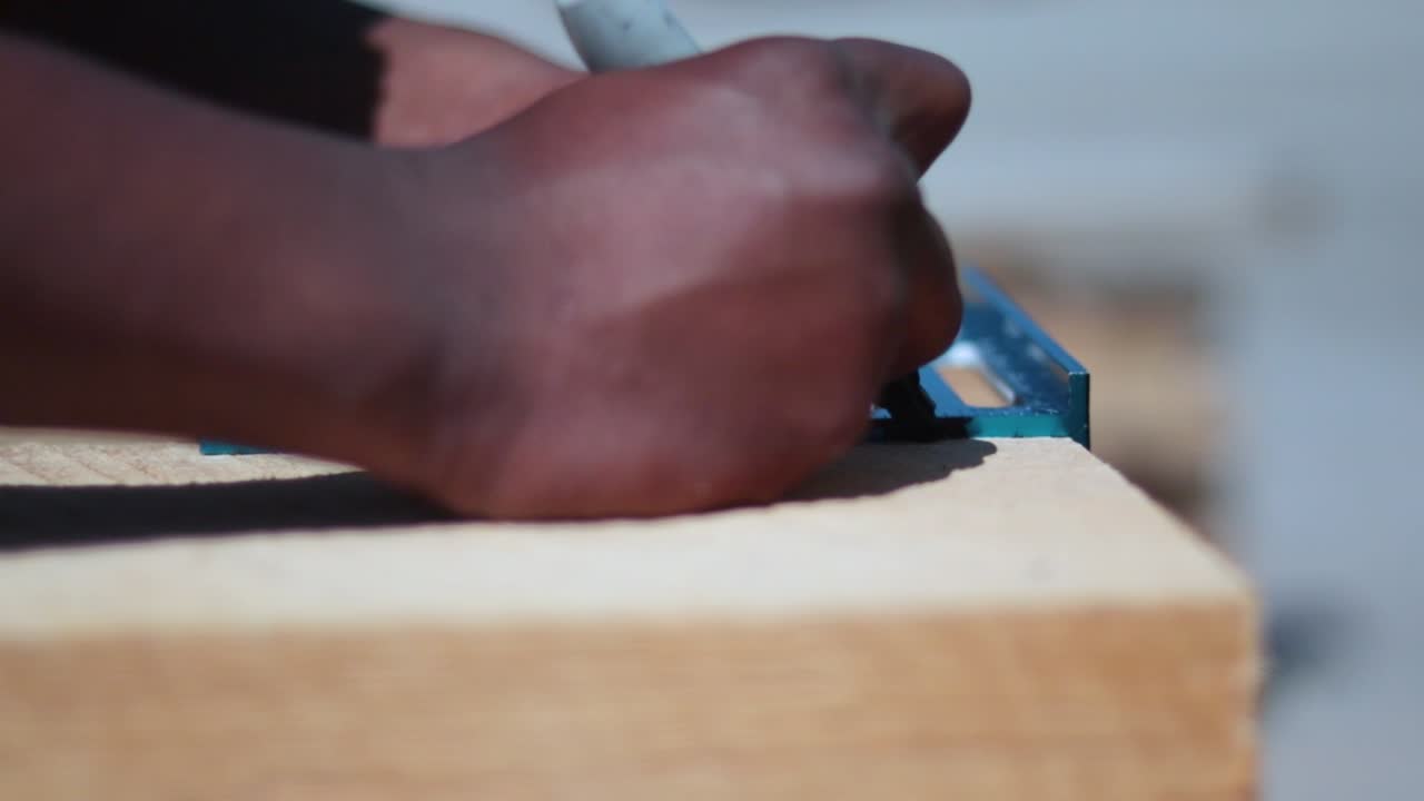 Two people of different ethnicities, black-African descent and white-Caucasian, are measuring and tracing a plank of wood. They are building raised beds.