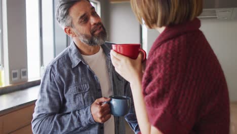 feliz pareja diversa en la cocina juntos bebiendo café y hablando