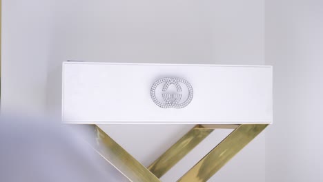 close up of luxury rectangular white bedside table with shiny stone logo, gold legs, in white bedroom