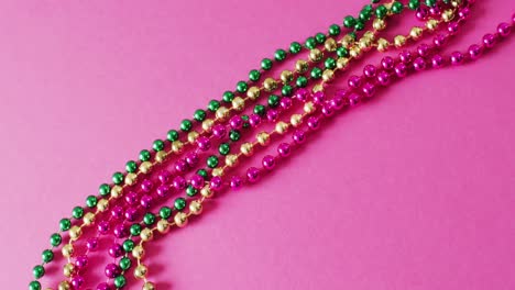 Video-of-pink,-gold-and-green-mardi-gras-carnival-beads-on-pink-background