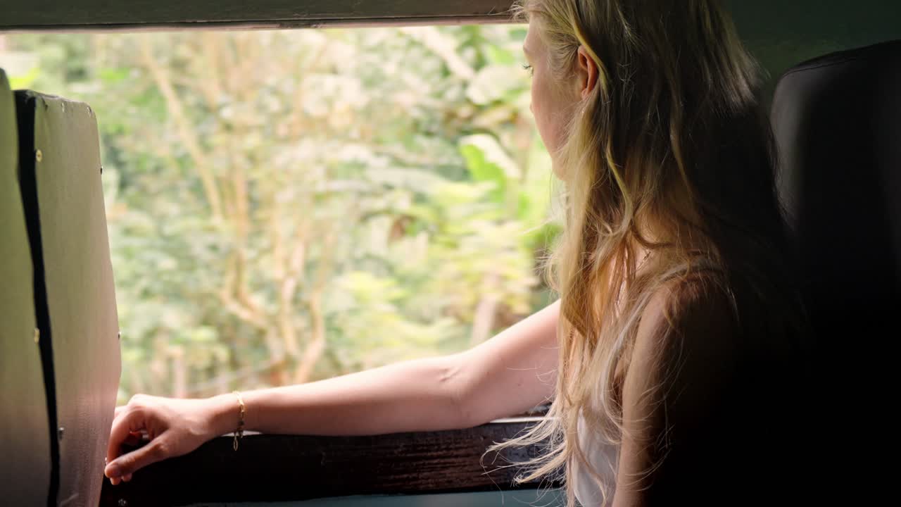 A female traveler sits by the window of a scenic train in Sri Lanka, watching the lush tropical jungle go by along the Ella–Kandy route.