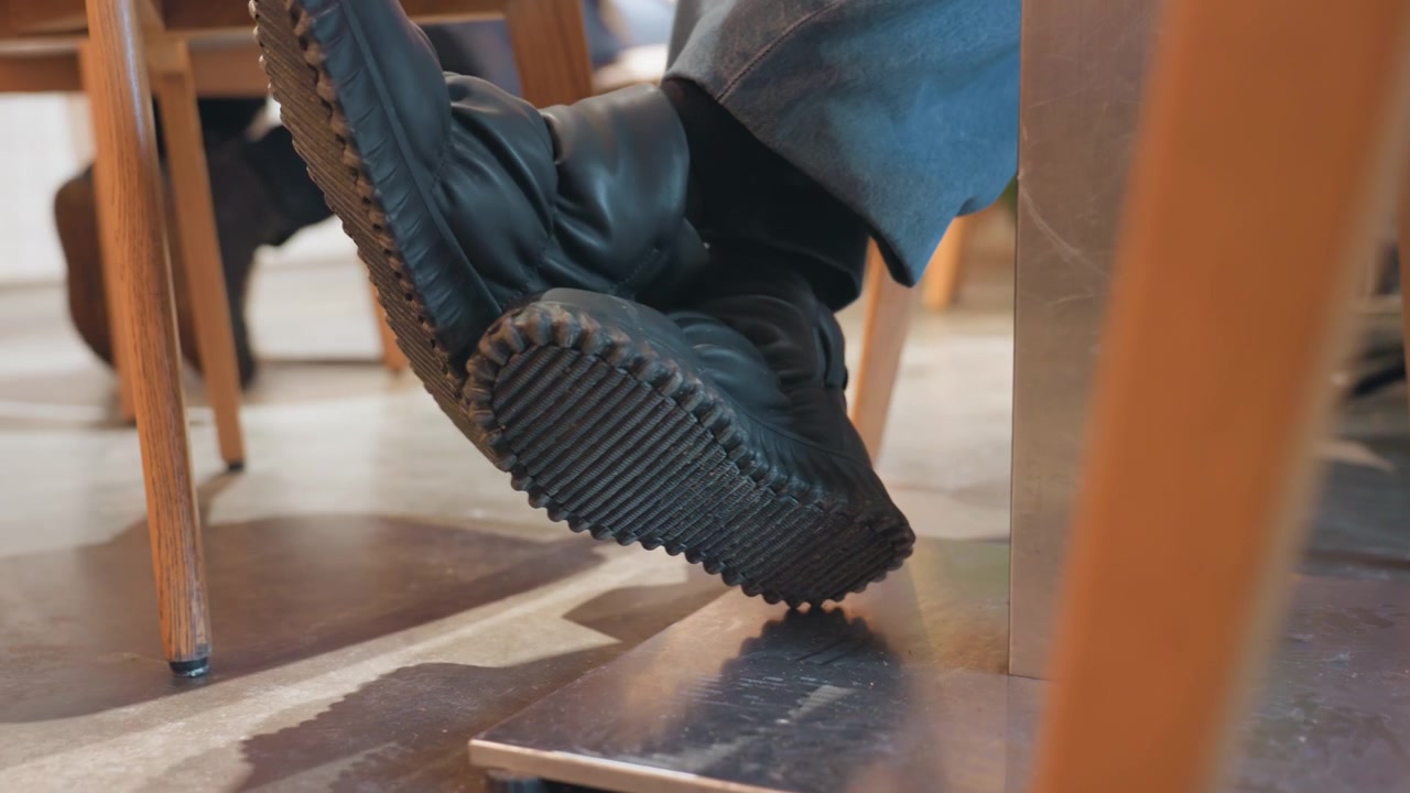 Close-up Sepatu Bot Hitam Seseorang Mengetuk Batang Logam di Bawah Meja