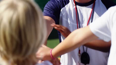 school kids and coach stacking hands in campus