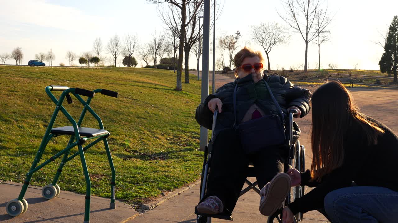 Enkelin stellt die Fußstütze des Rollstuhls für die Oma ein, bevor sie im Park spazieren geht.