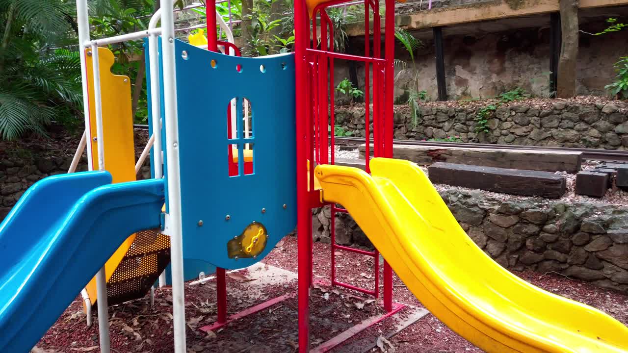 Colorful children’s dual slides and climbing bars surrounded by trees and stone walls near Parque Chapultepec, Morelos.